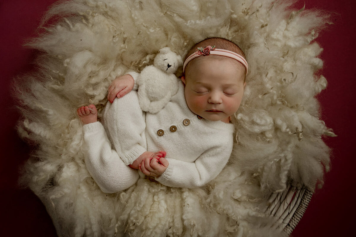 A newborn baby in a white onesie sleeps with a tiny bear in a woven basket on a blanket after mom found parenting classes in springfield, il