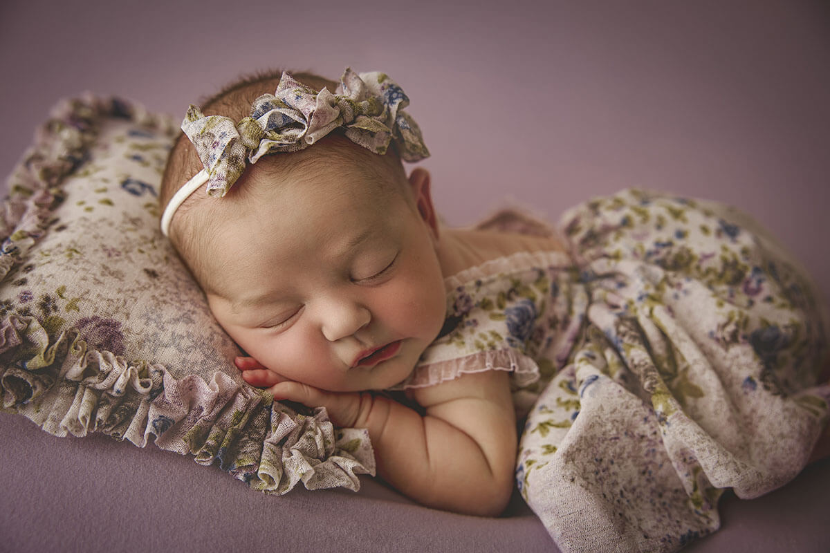 A sleeping newborn baby girl in a floral print dress on a matching pillow after mom found parenting classes in springfield, il