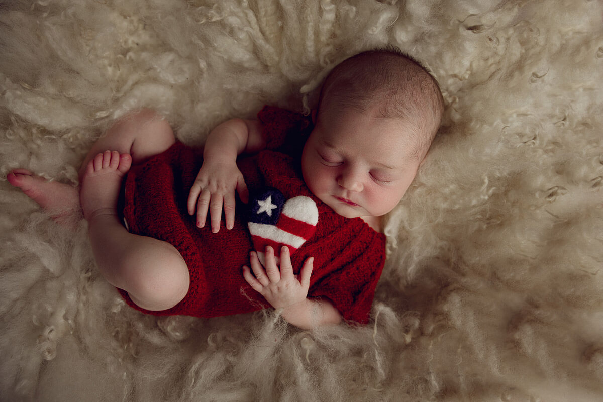 A sleeping newborn in a red knit onesie holding a tiny felt heart on a fluffy blanket after mom did prenatal yoga in springfield, il