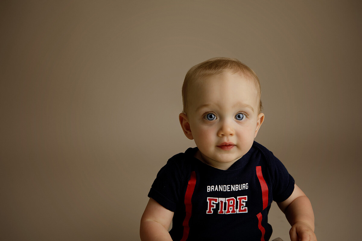 A closeup of a happy baby in a firefighter shirt in a studio