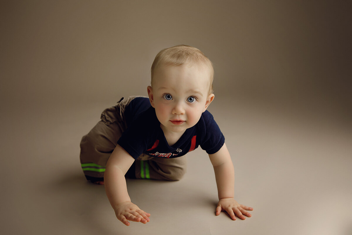 An infant crawls on the floor of a studio while looking up with blue eyes before visiting a pumpkin patch in Springfield, IL