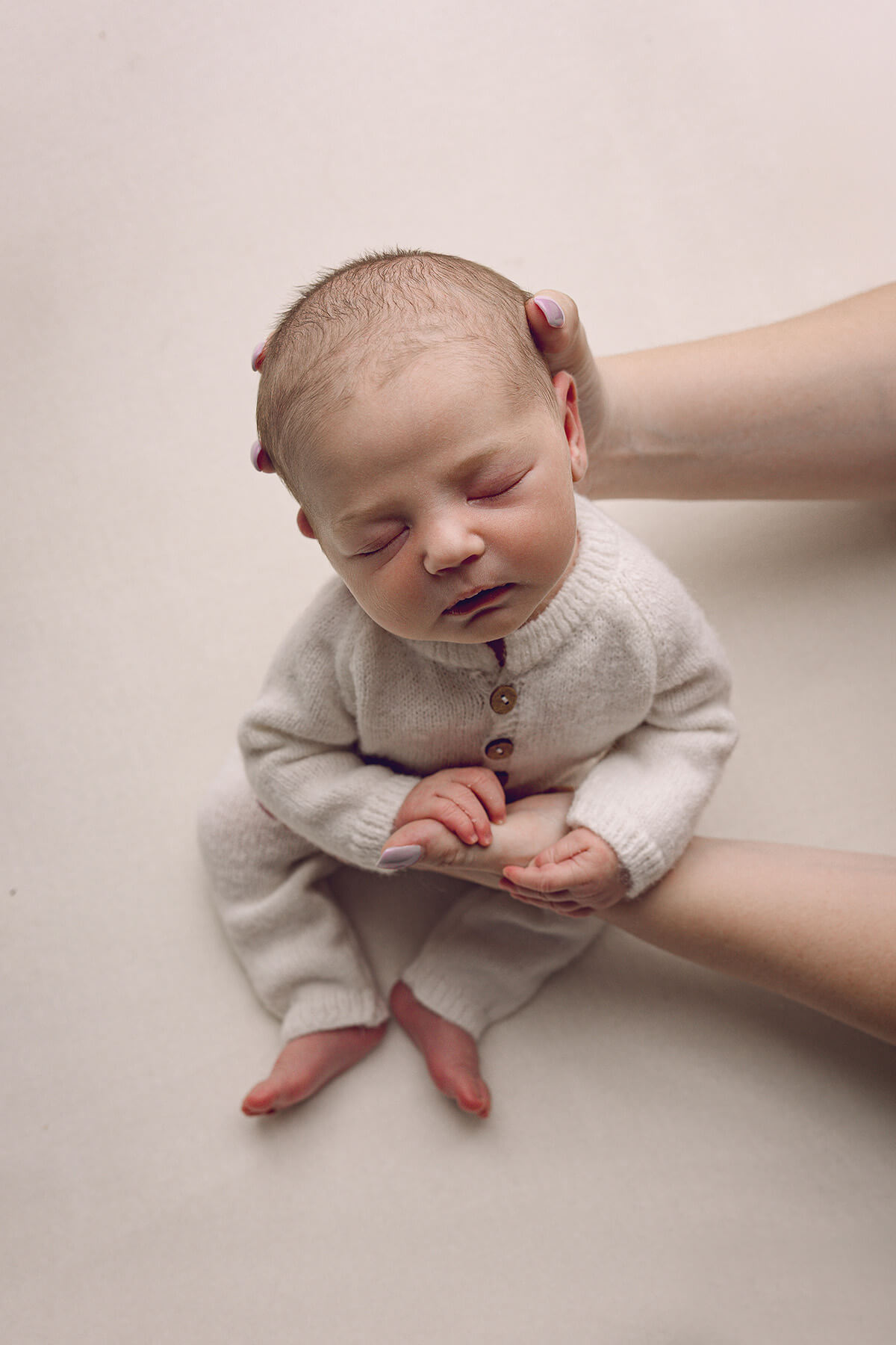 a sleeping newborn baby is held up by mom in a white onesie in a studio after leaving birth center of bloomington normal