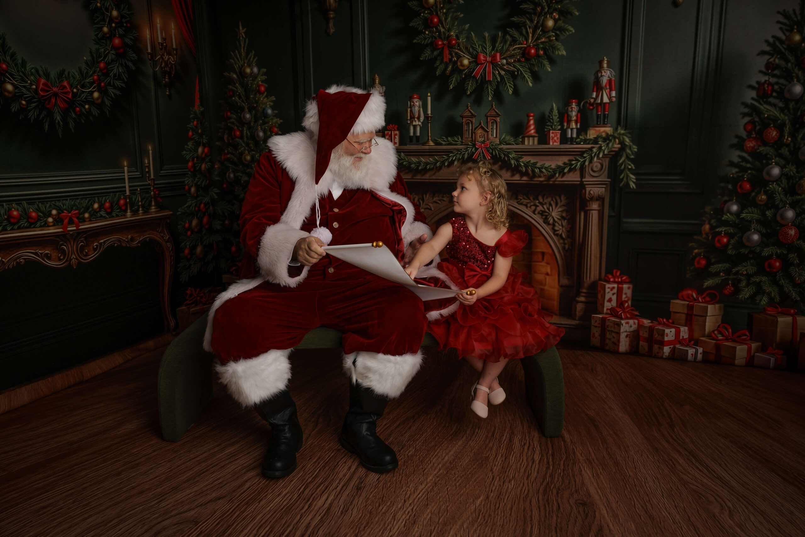 santa shows a young girl his nice list on a bench in a studio