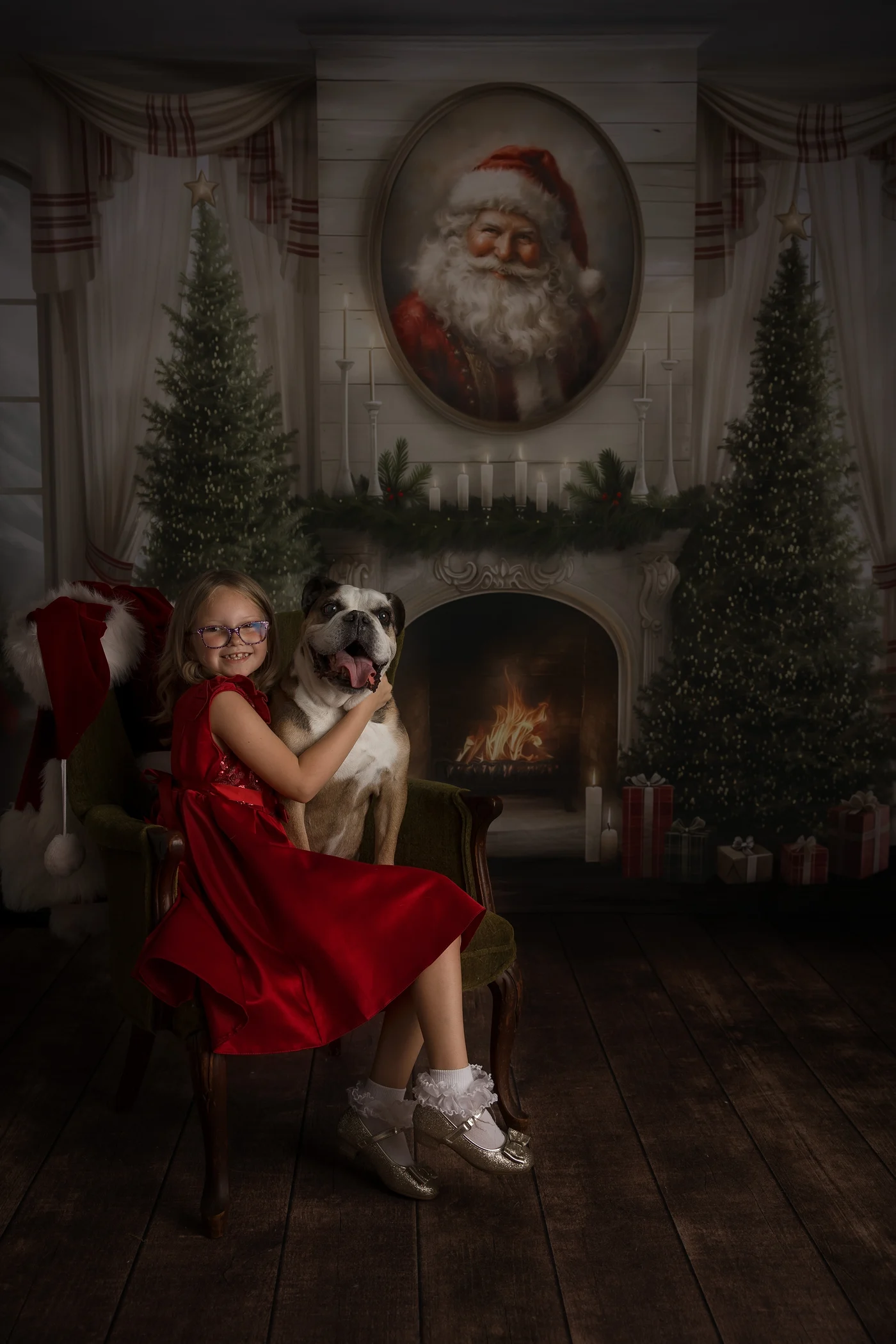 a happy young girl sits in an antique chair in a red dress hugging her smiling bulldog sitting with her in front of christmas trees in springfield il