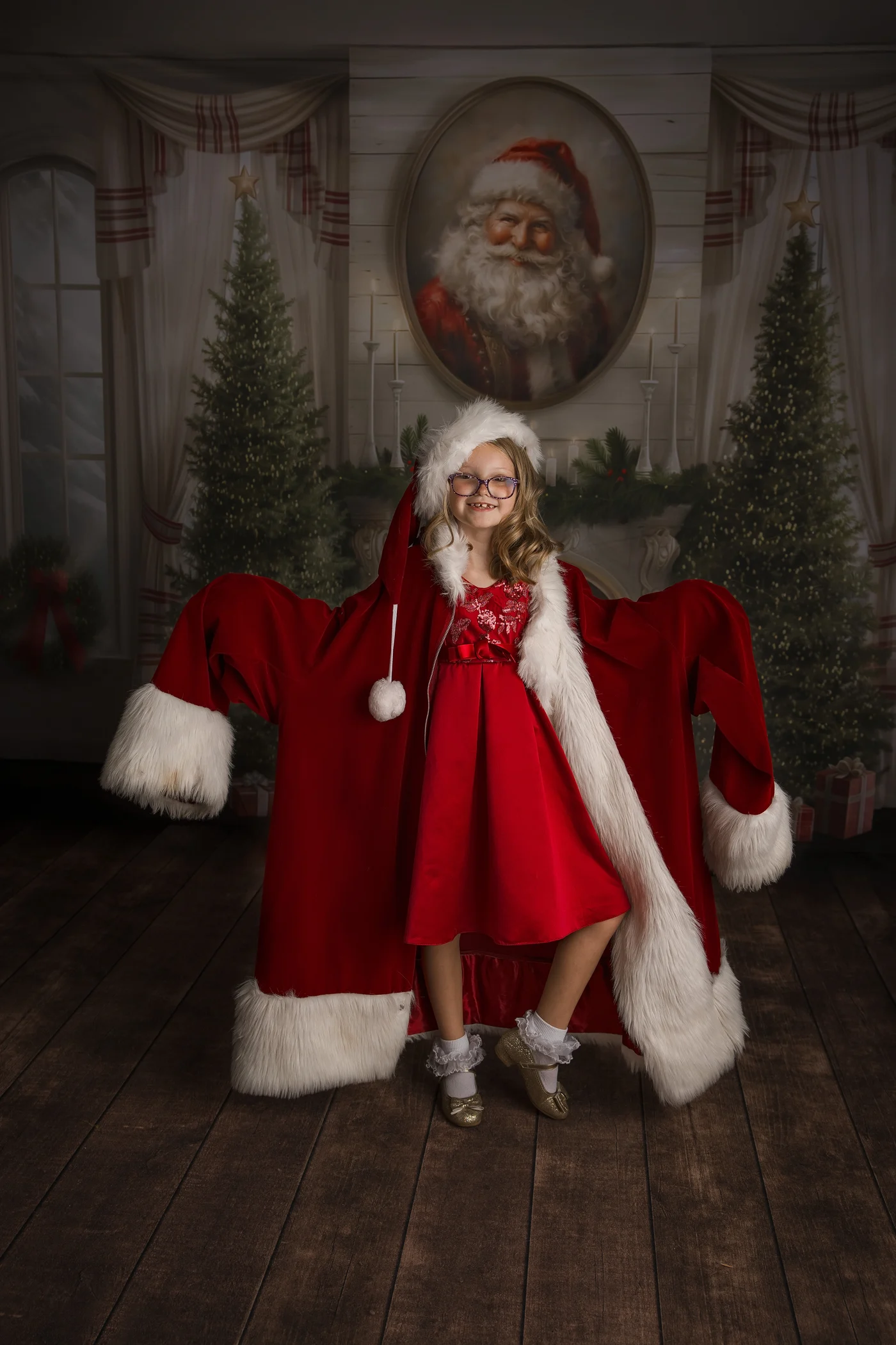 A smiling young girl stands in a studio wearing an oversized santa jacket in front of christmas trees in springfield il