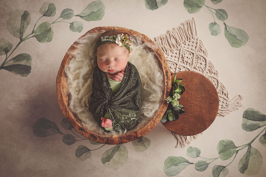 A sleeping newborn in a wooden bowl wrapped in a sage lace blanket after visiting daycares in bloomington il