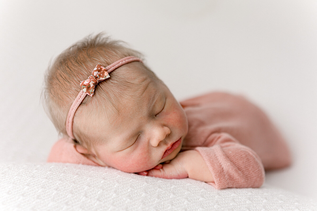 A sleeping newborn baby girl in a pink onesie and matching bow headband thanks to a midwife in bloomington il
