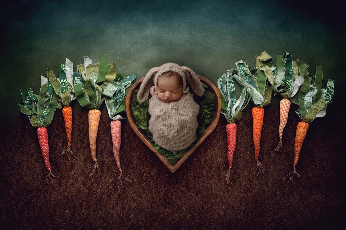 A sleeping newborn in a knit bunny onesie surrounded by fabric carrots after getting 3d ultrasound in bloomington il