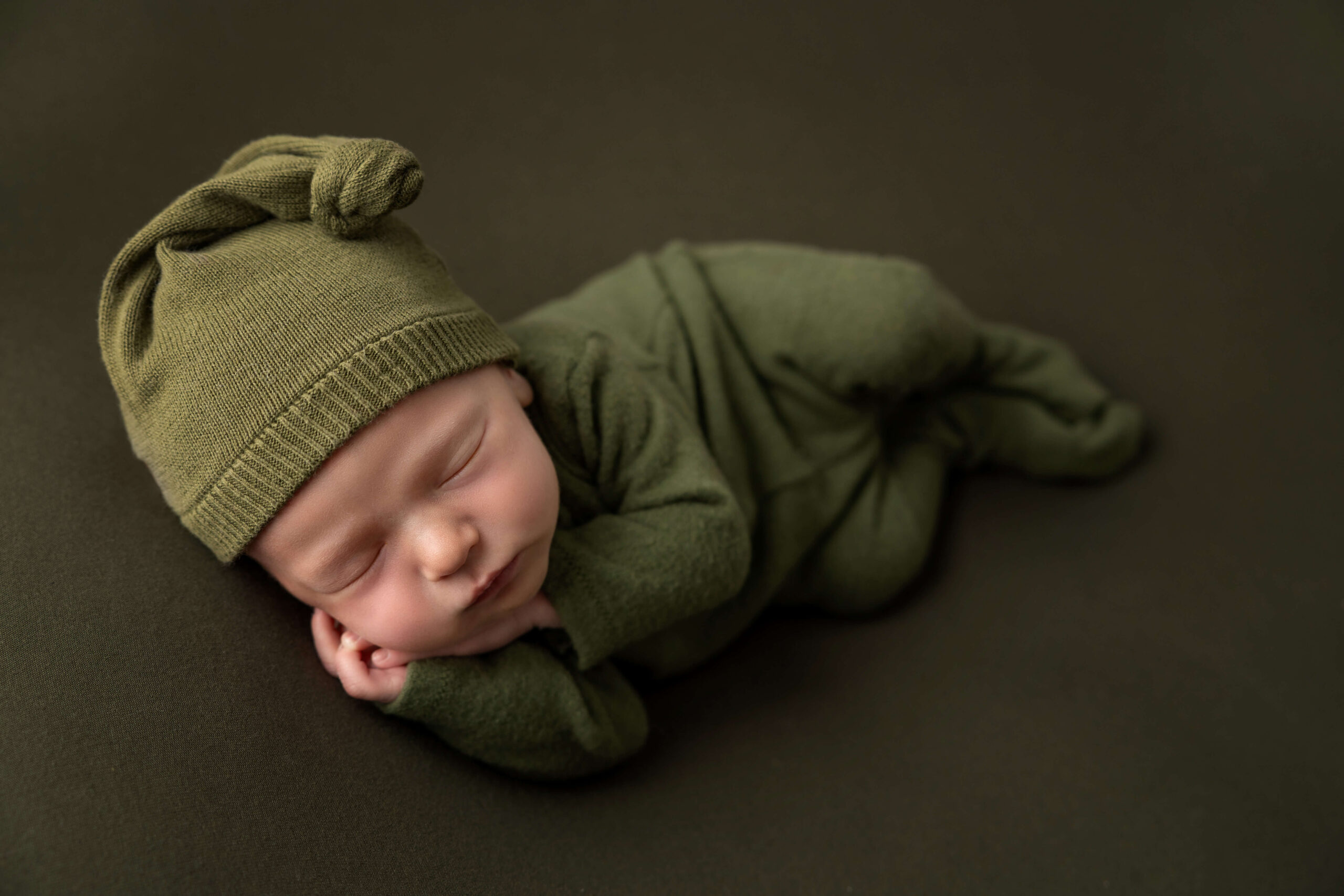 A newborn baby sleeping in a green onesie and matching sleep cap on his side