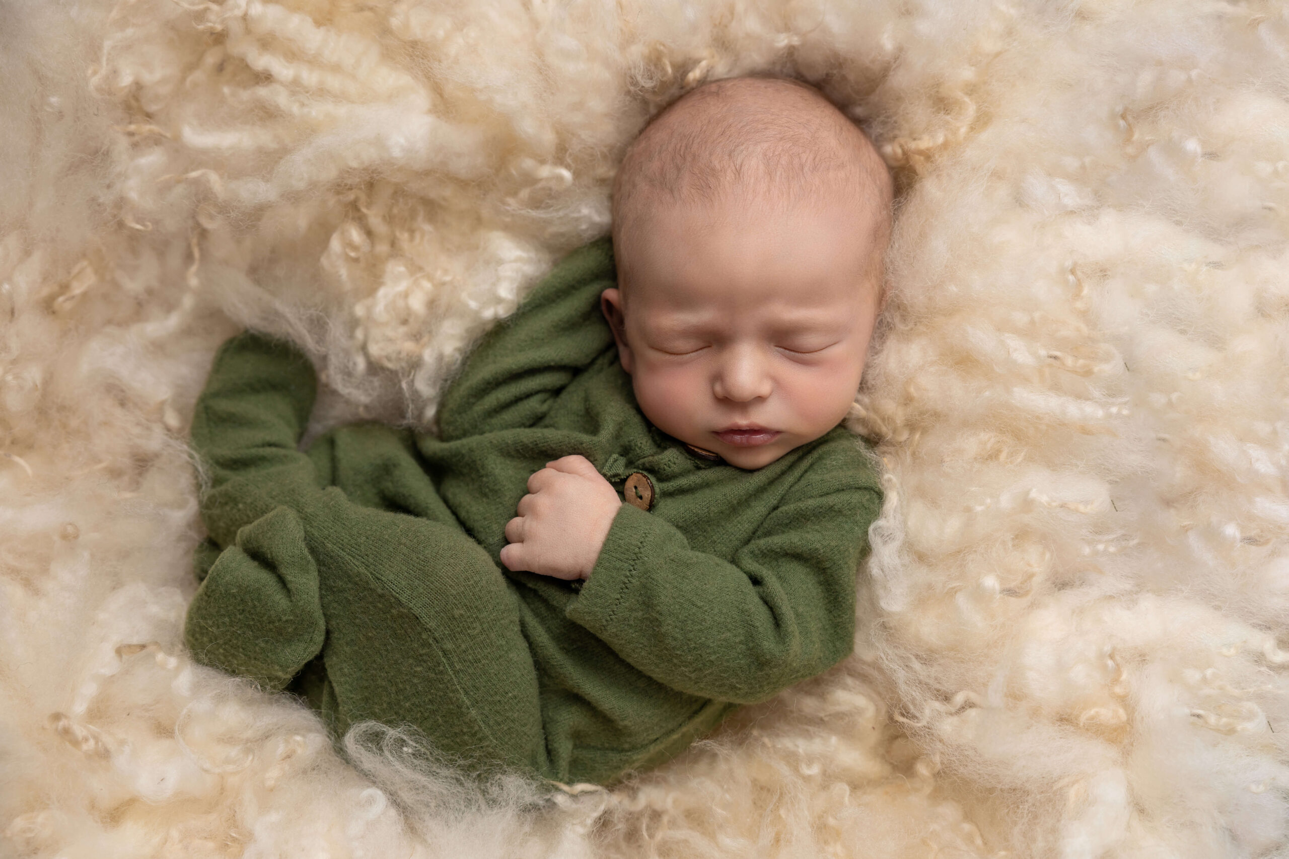 A newborn baby sleeps in a green onesie on a fluffy blanket after using baby shower venues in bloomington il