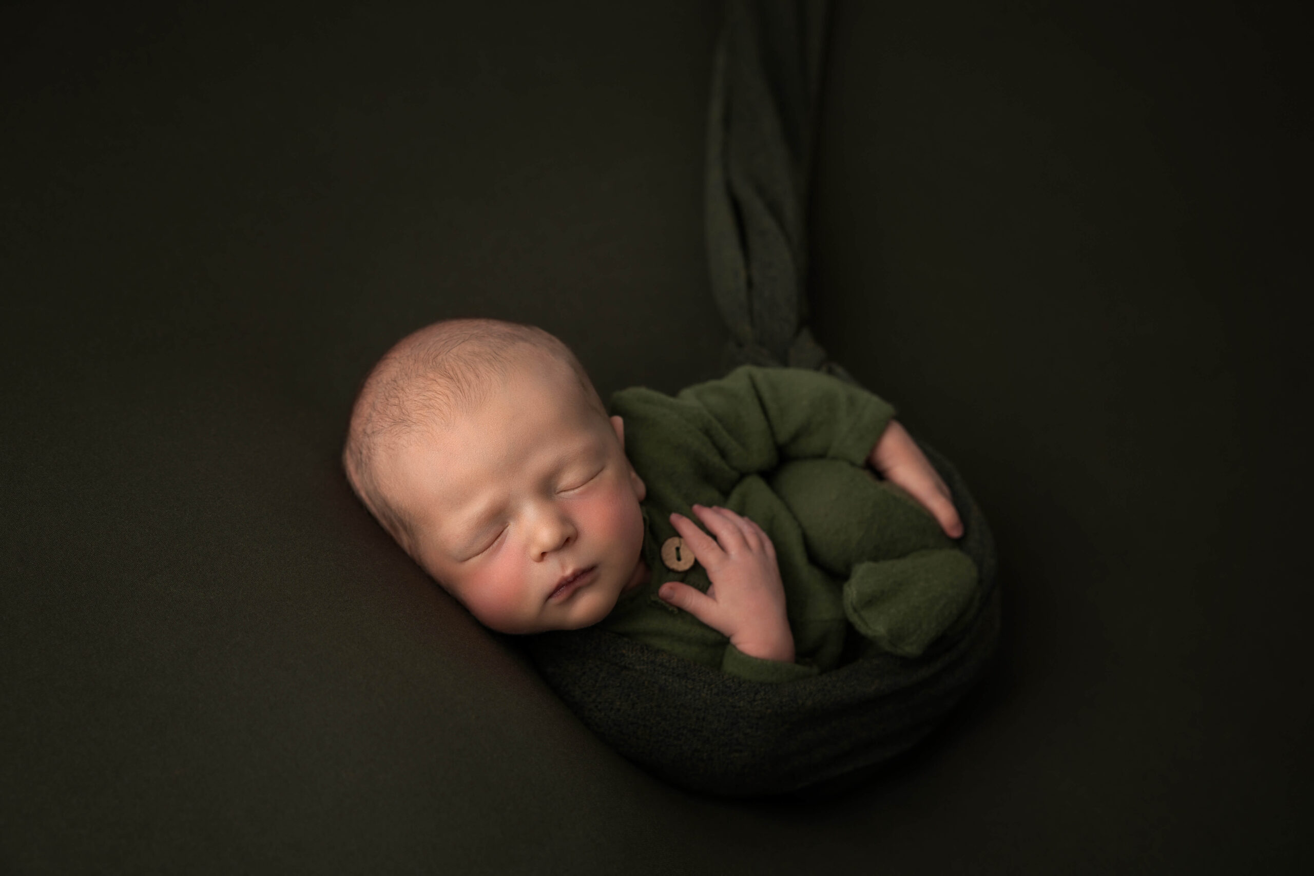 A newborn baby sleeps in a green onesie with a hand on his chest after using baby shower venues in bloomington il