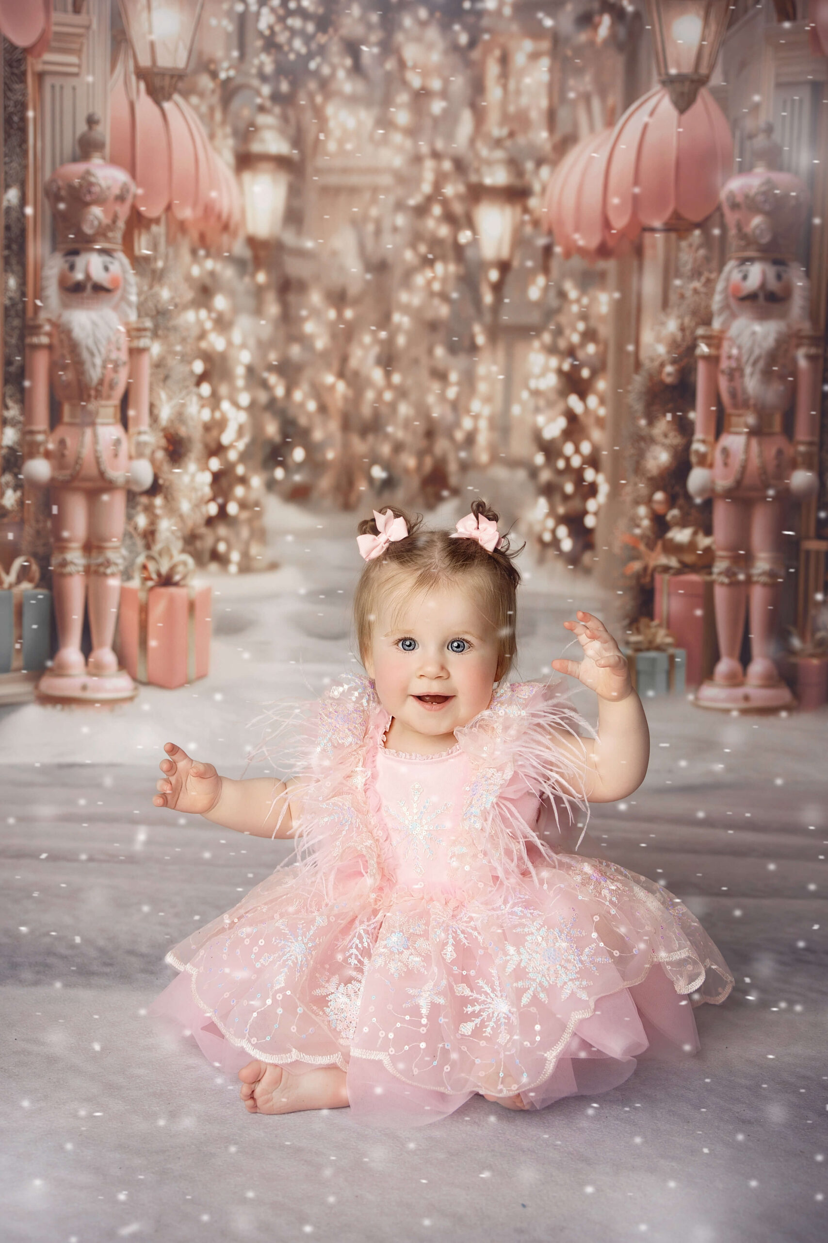A happy girl in a pink gown sits with nutcracker backdrop as snow falls around her with a big smile