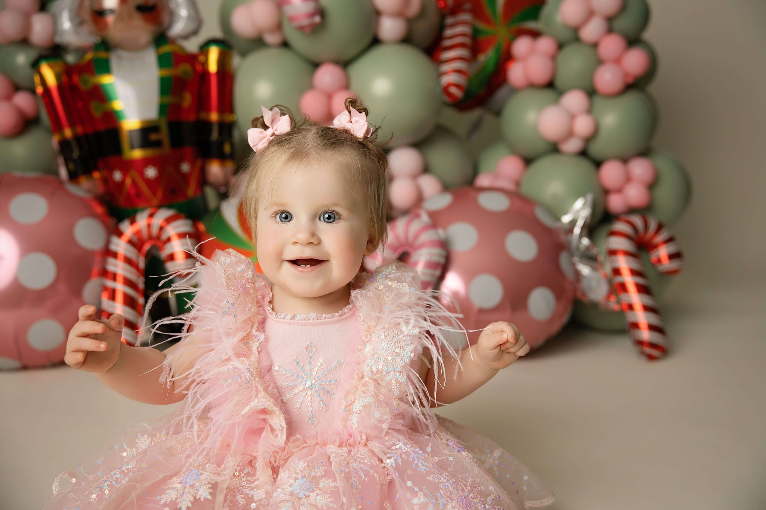 A giggle baby girl with pigtails in a pink frilly gown sits in front of christmas candy cane balloons after visiting baby stores in bloomington il