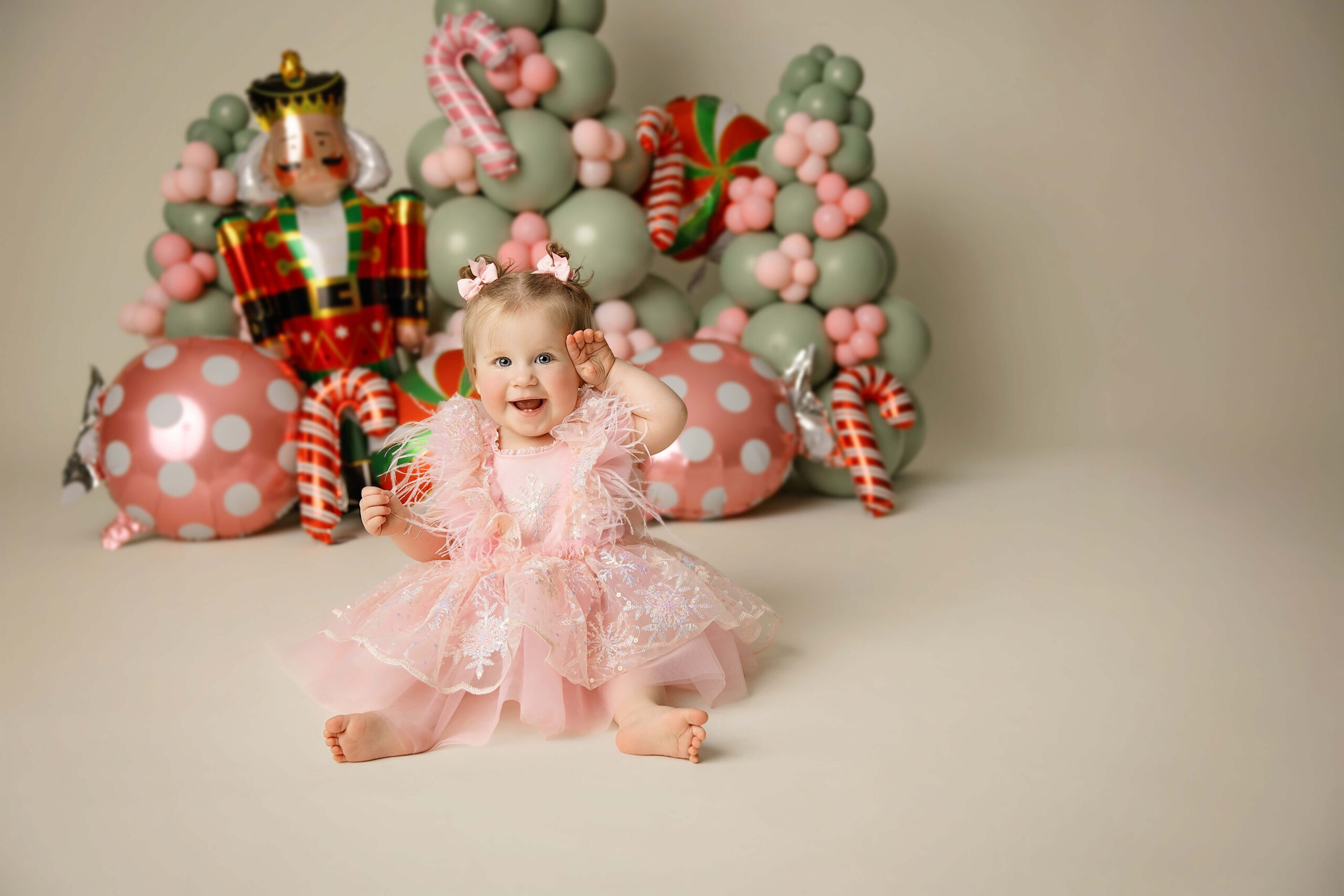 A giggling baby girl in a pink gown sits on a christmas themed studio floor with a big smile after visiting baby stores in bloomington il