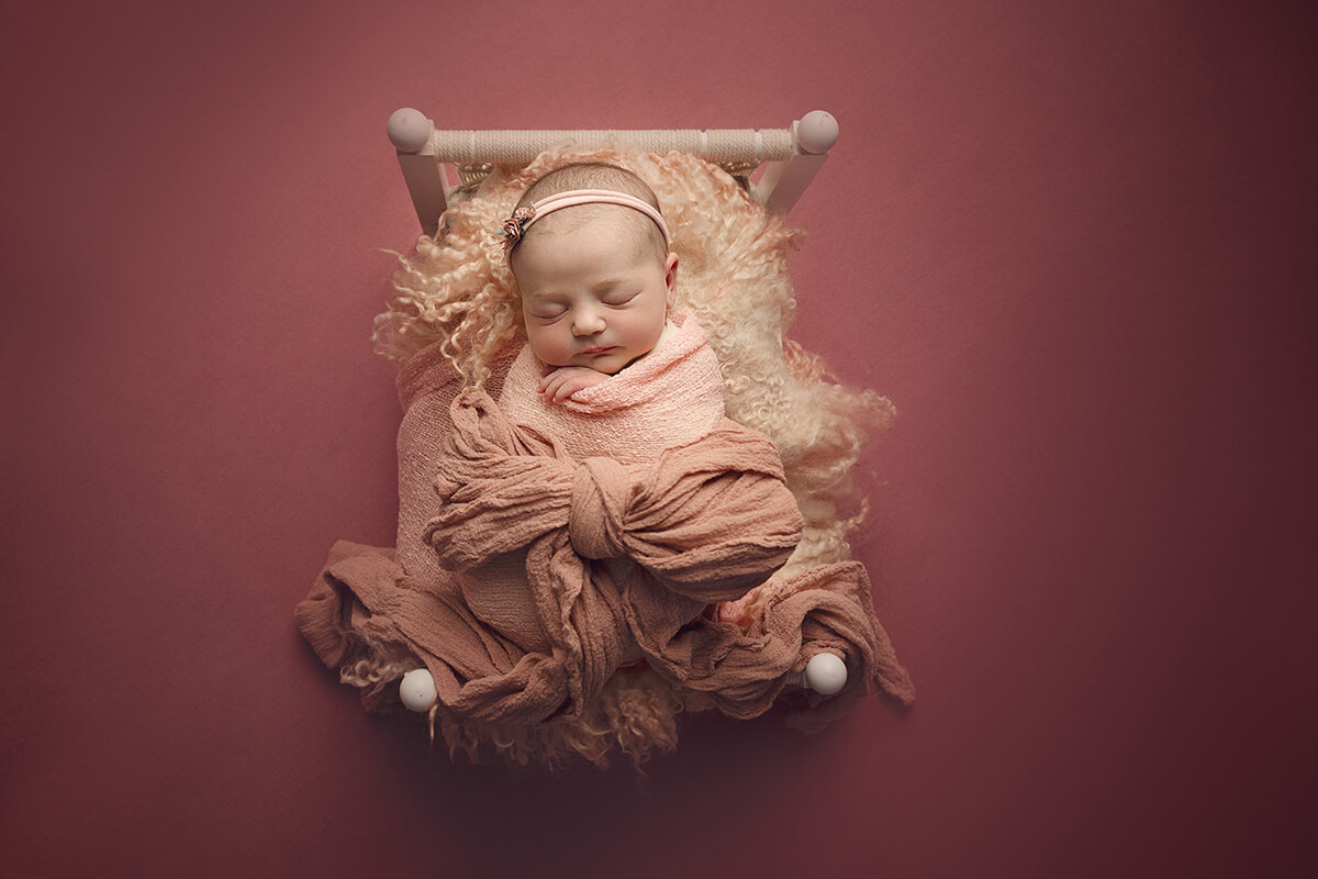 A peaceful sleeping newborn girl in a pink swaddle with a bow on her belly sleeps in a tiny bed in a studio thanks to ivf in Springfield, IL
