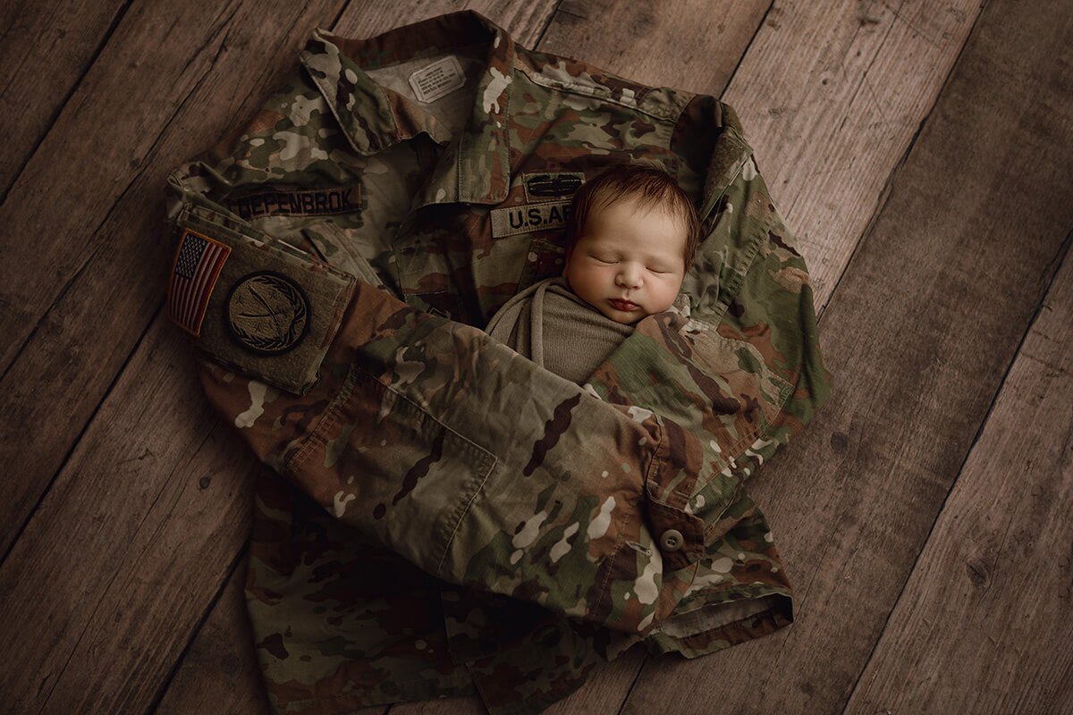 A newborn baby in a forest green swaddle sleeps wrapped in a US Arm BDU thanks to ivf in Springfield, IL