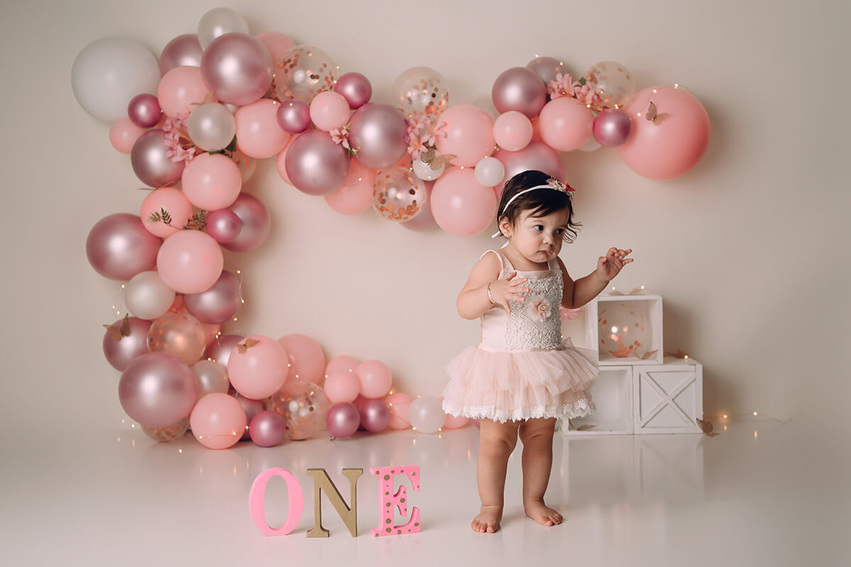 A toddler girl in a pink dress plays in a birthday themed studio with one after visiting pediatric dentists in bloomington il