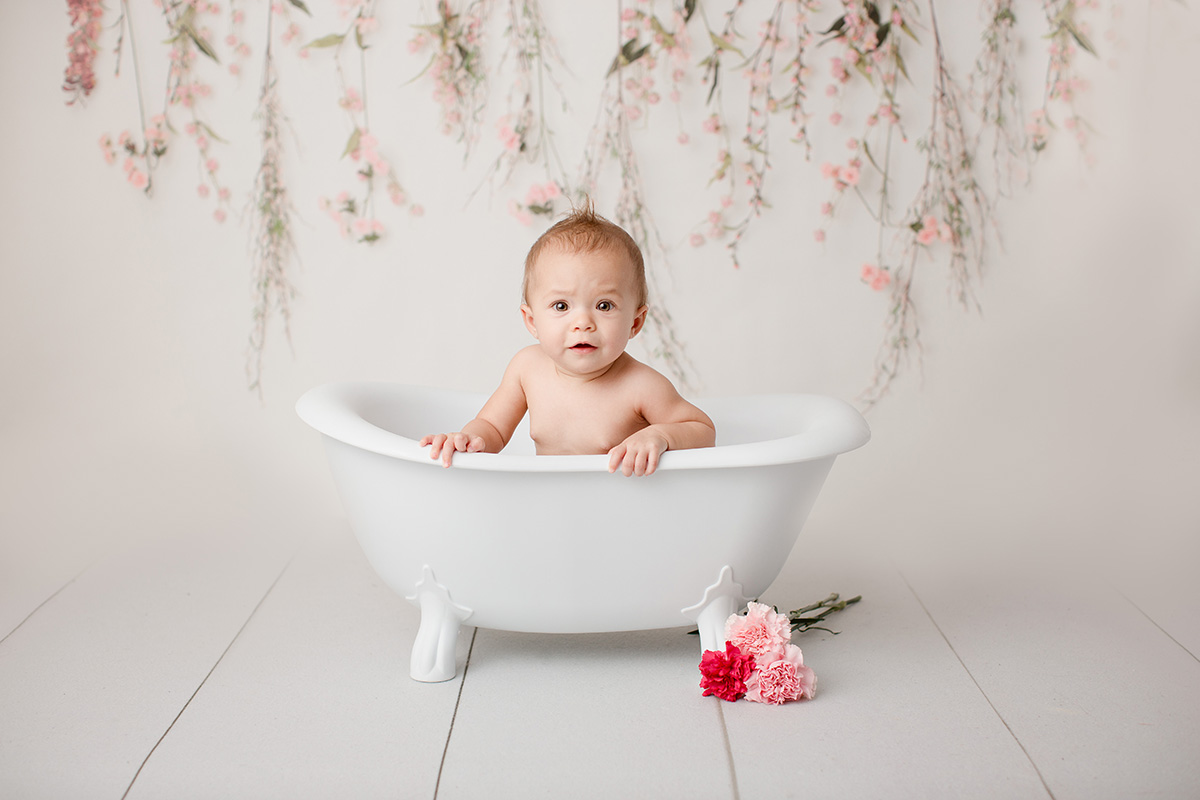 a baby sits in a tiny bathtub looking and leaning on the edge