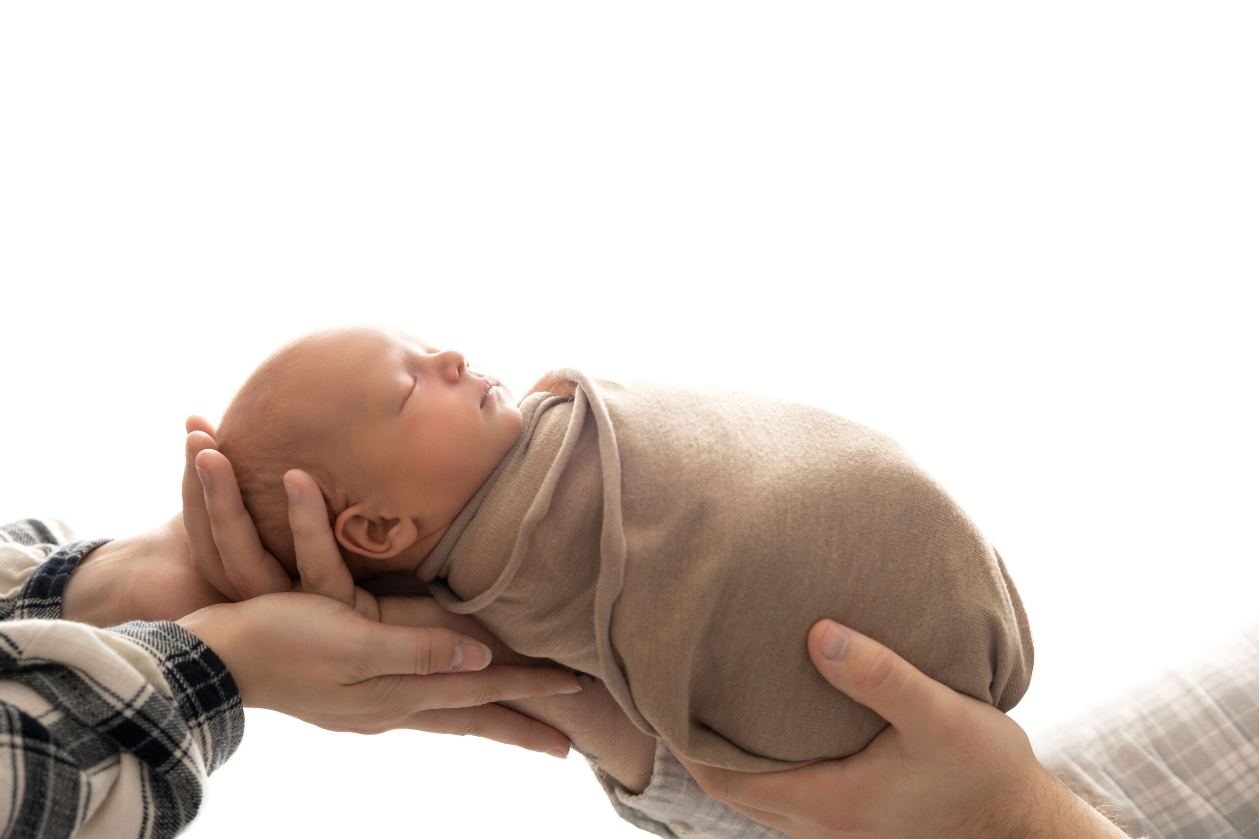 a sleeping newborn baby in a tan swaddle in mom and dad's hands