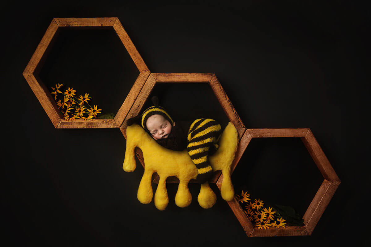 a newborn baby in a black and yellow knit onesie sleeps in honeycomb wall hangers on a honey bed thanks to prenatal yoga in Bloomington, IL