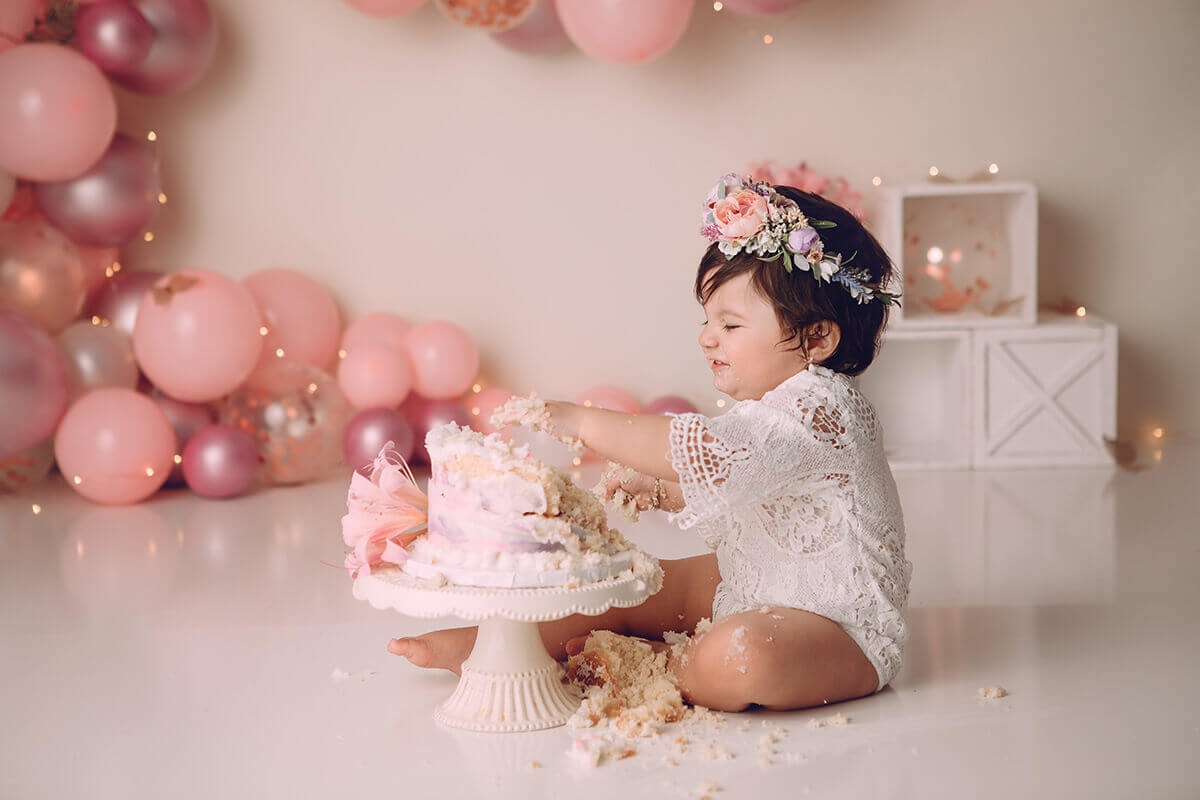 A giggling baby girl in a white lace onesie smashed a pink cake in a studio thanks to bakeries in springfield il
