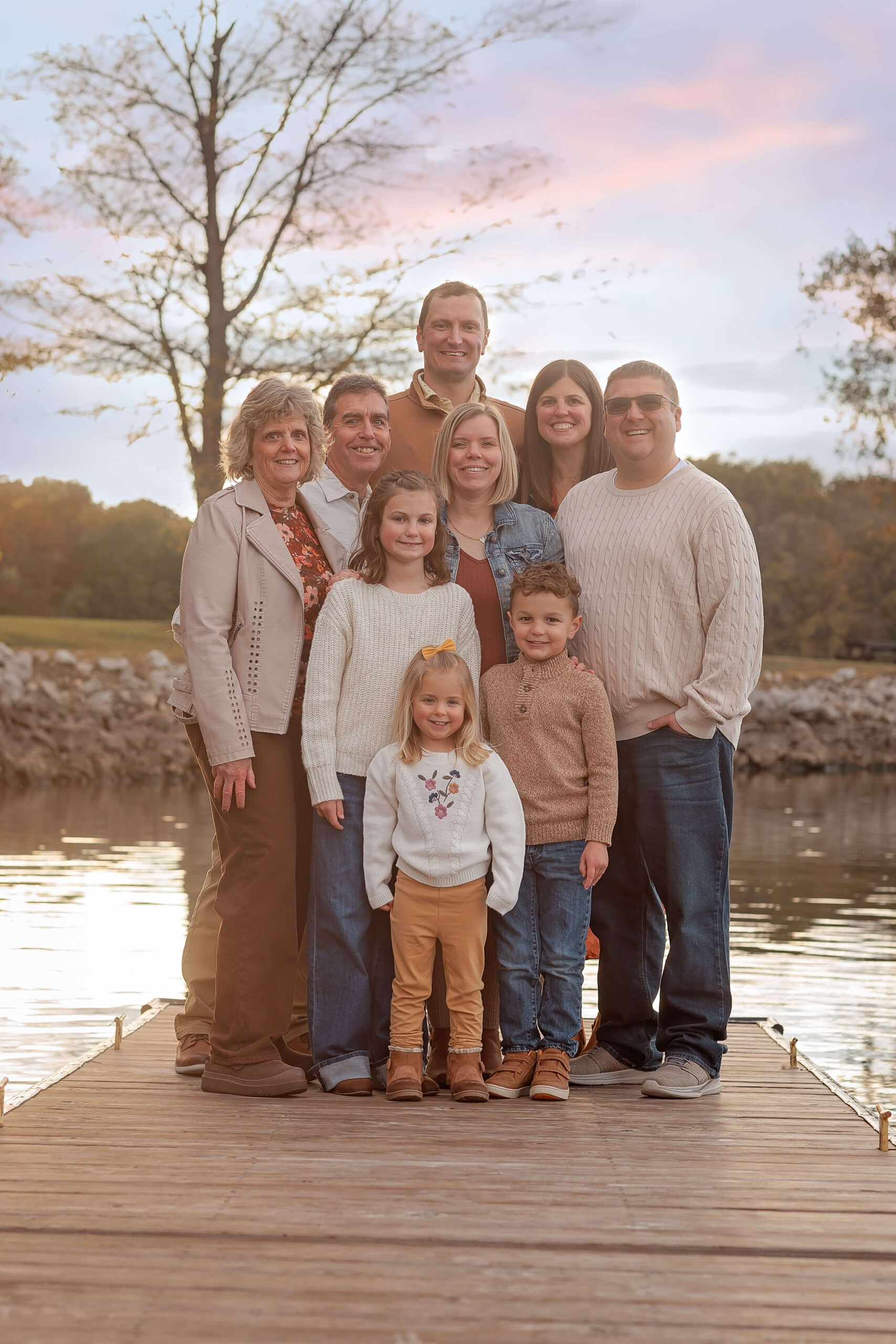 A happy family stands on a dock smiling at sunset with three young children