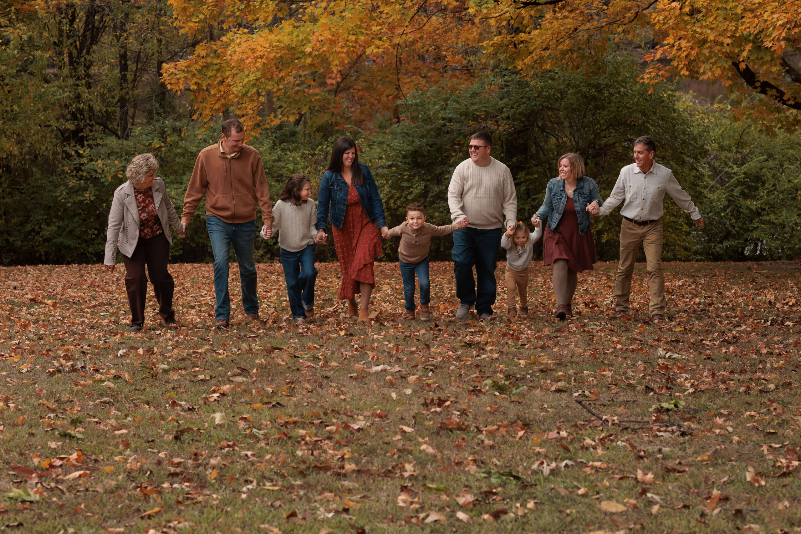 An extended family laughs while walking in a park in fall holding hands after visiting the children's discovery museum