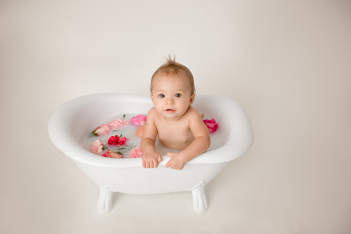 A happy baby plays in a bathtub filled with pink flowers before putting on daisy diapers