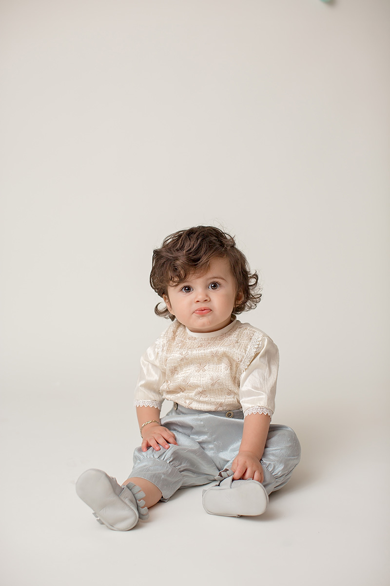 A baby girl in blue pants sits on the floor of a white studio after enjoying daisy diapers