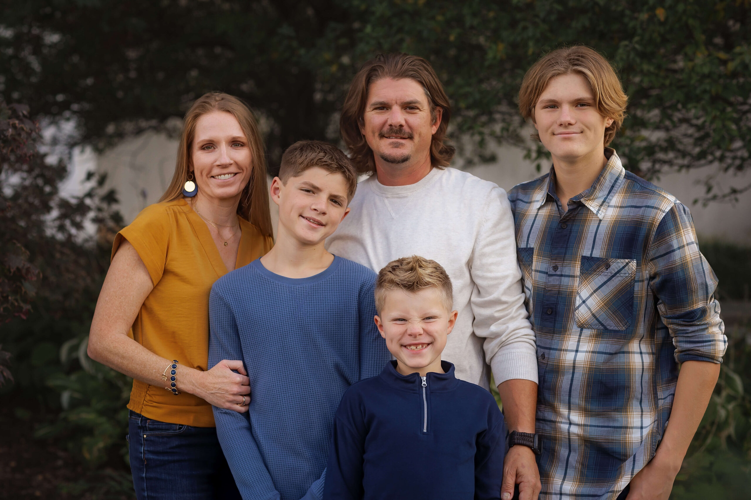 Three teen sons in blue outfits stand smiling witht heir mom and dad in a park
