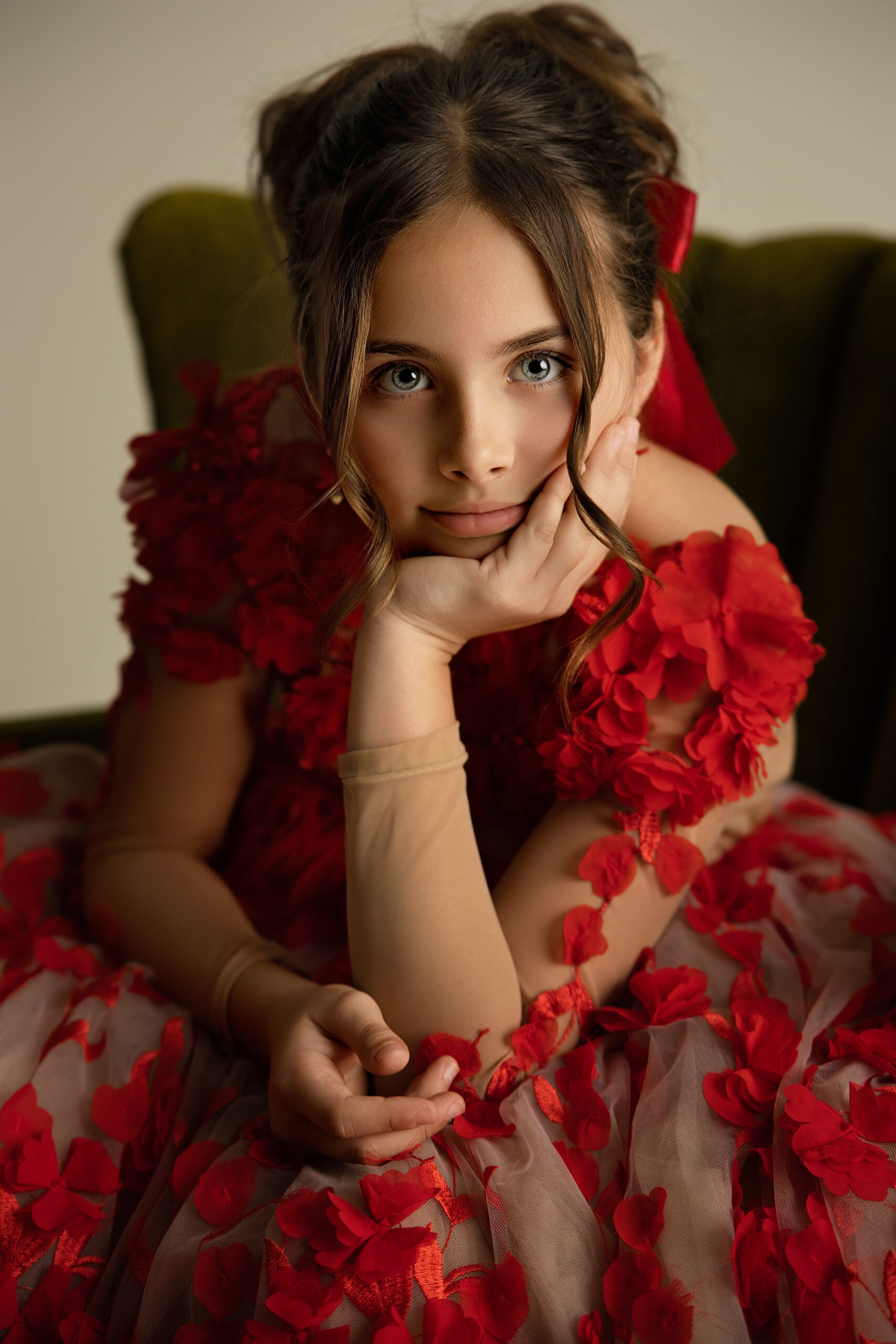 A closeup of a young girl leaning on her knee in a red flower gown