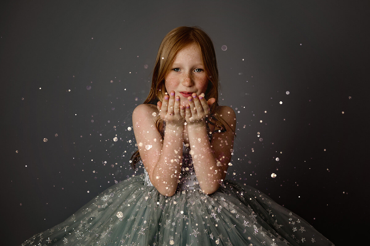 A young girl in a blue gown blows glitter in front of her before visiting kid-friendly restaurants in Bloomington, IL