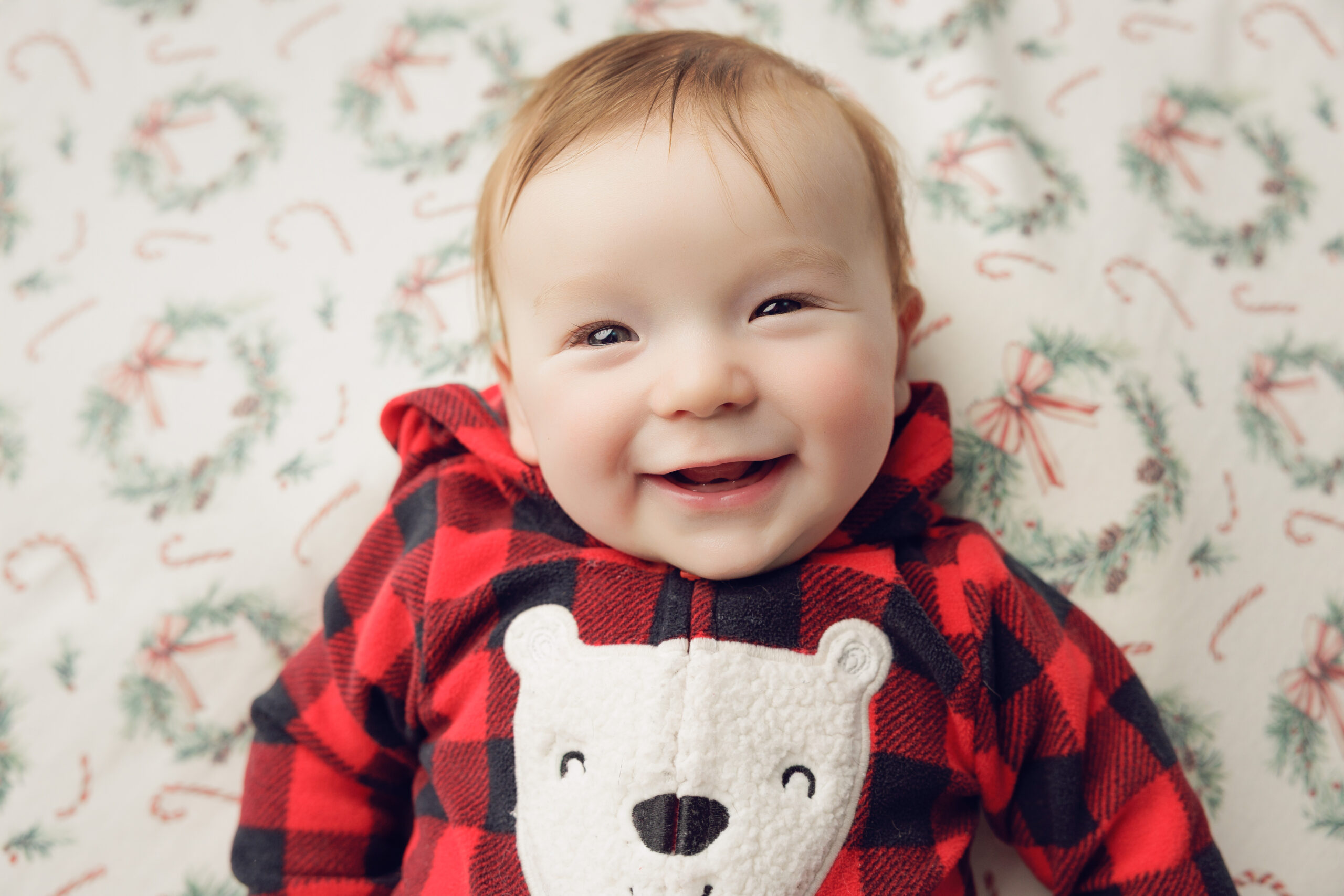 A giggling infant lays on a christmas bed in red plaid pajamas after some fun mommy and me classes in bloomington il
