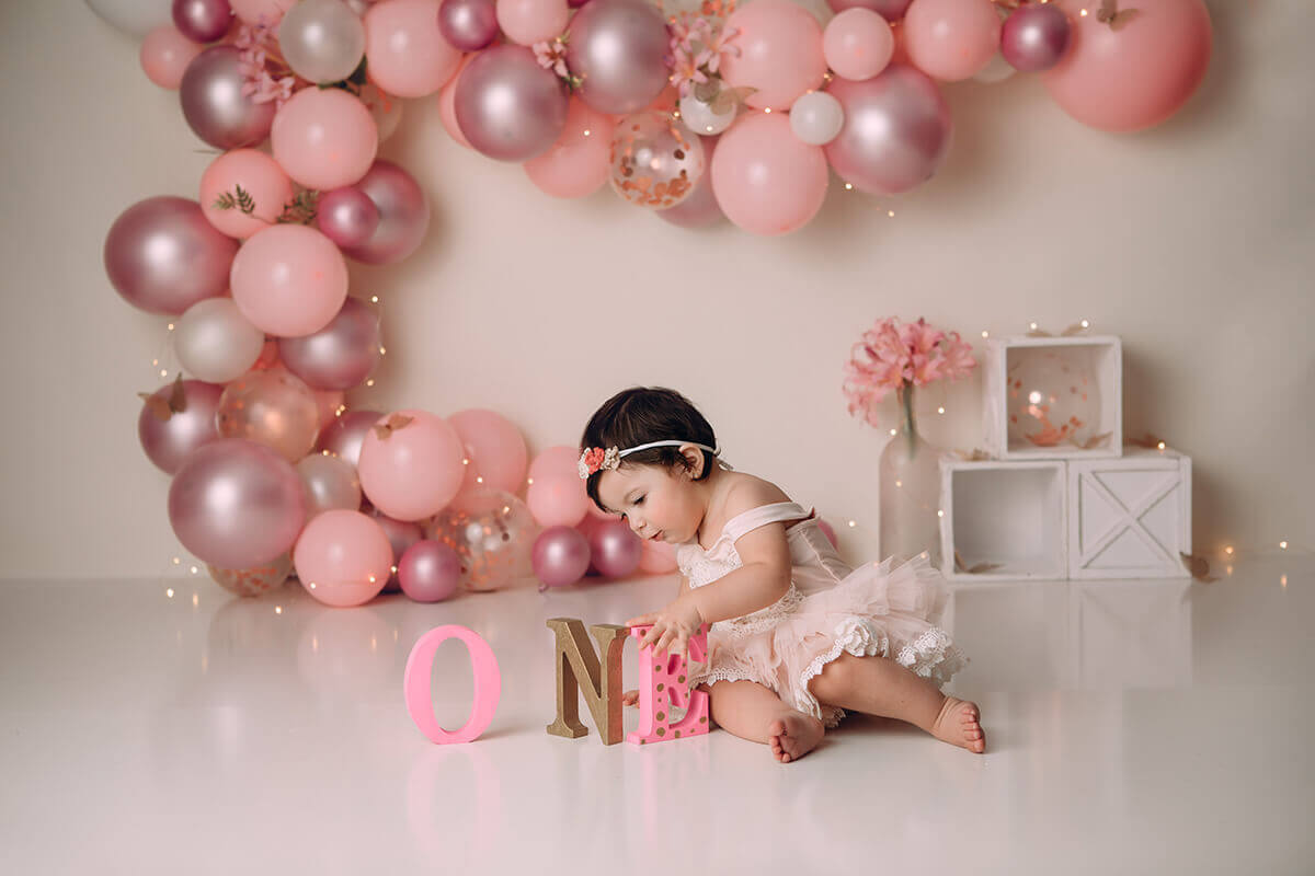 A baby girl in a pink dress plays with letters spelling one in a studio for her birthday after exploring montessori children's centre