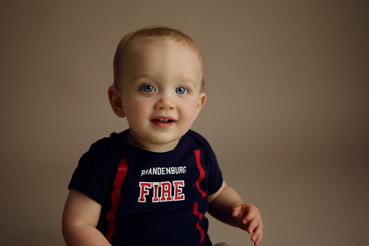 A happy toddler in a fire fighter shirt smiling in a studio