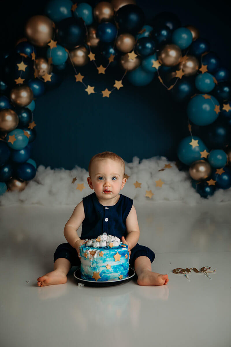 A happy baby sits in a studio straddling a blue decorated cake with stars after finding preschools in bloomington il