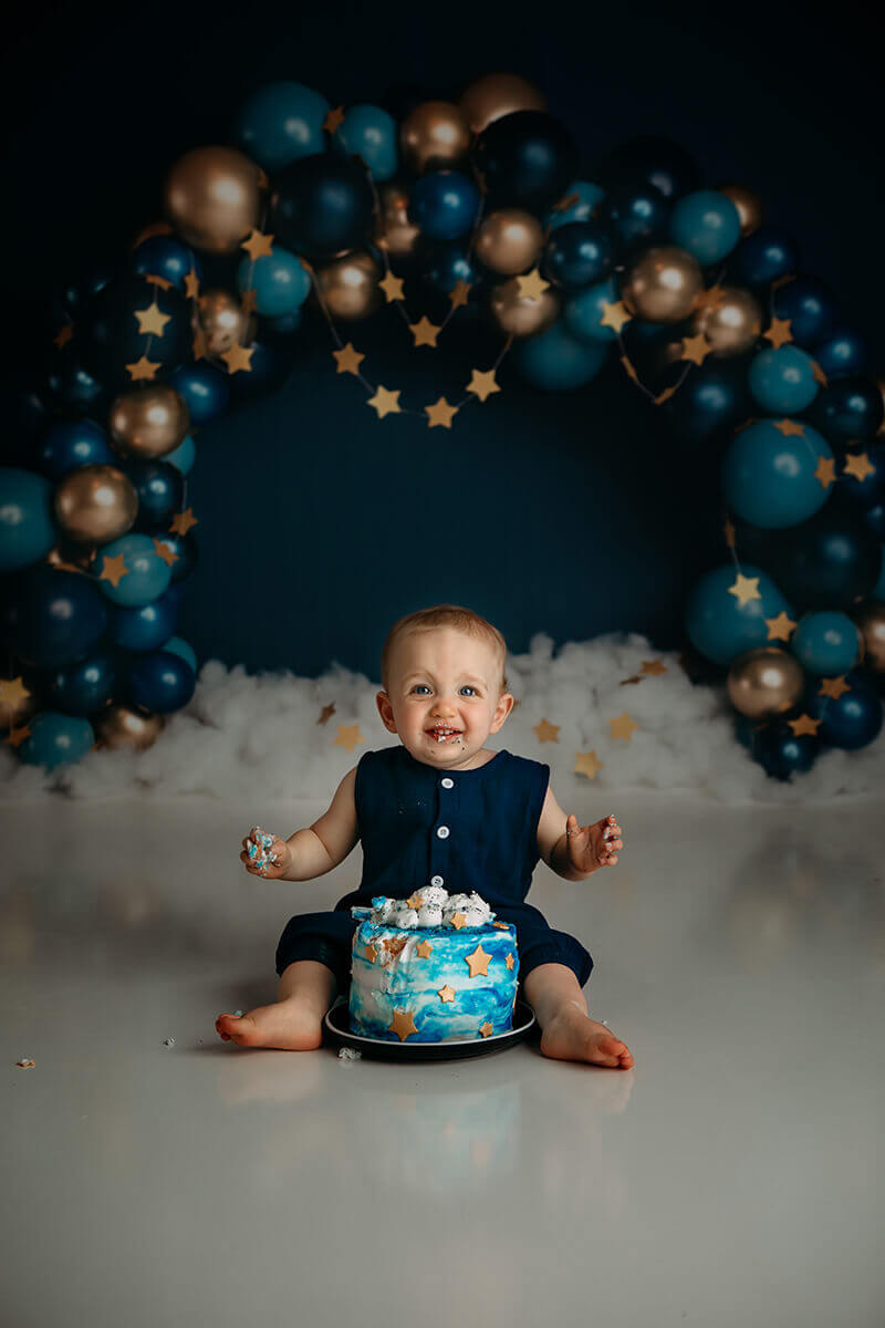 A toddler in a blue onesie sits behind a star decorated cake in a studio before attending preschools in bloomington il