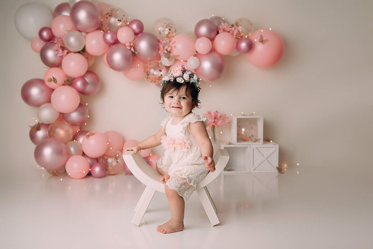 A toddler girl in a pink dress plays on a curved stool in a pink studio before some fun things to do with kids in bloomington, IL
