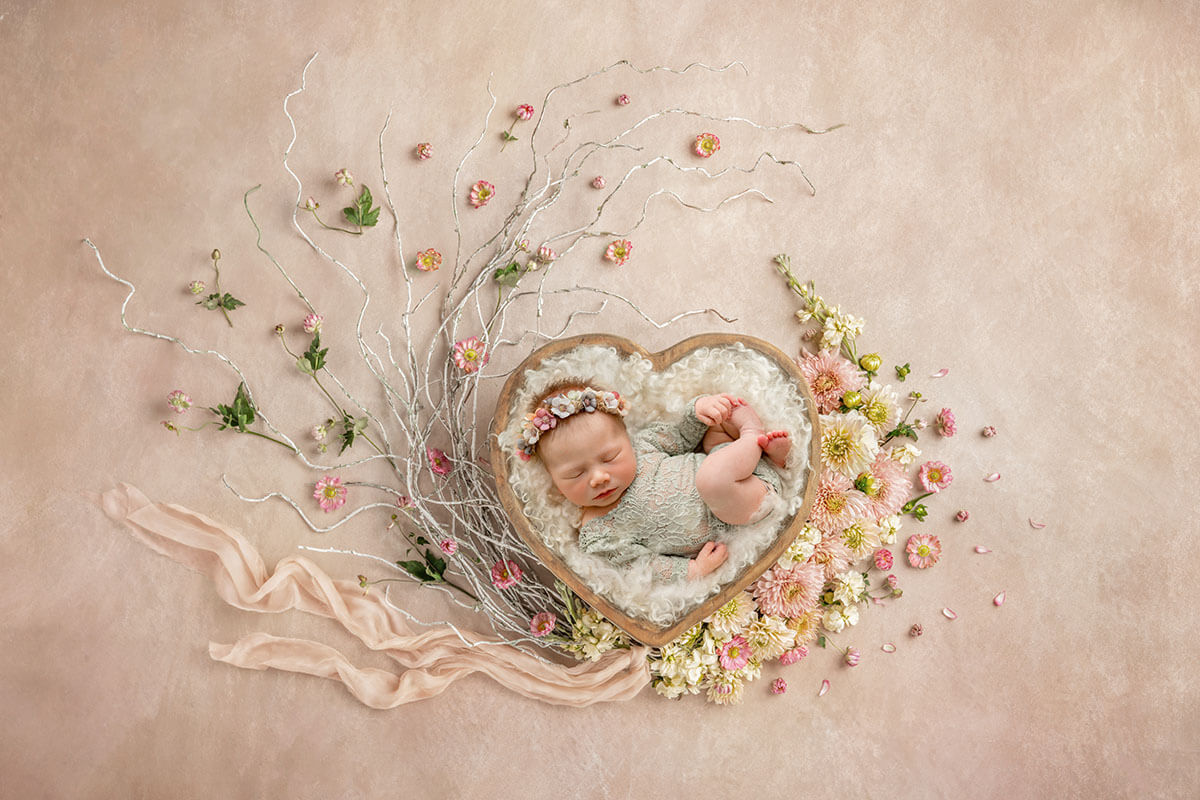 A newborn baby girl sleeps in a heart shaped bowl surrounded by flowers after finding pediatricians in peoria il