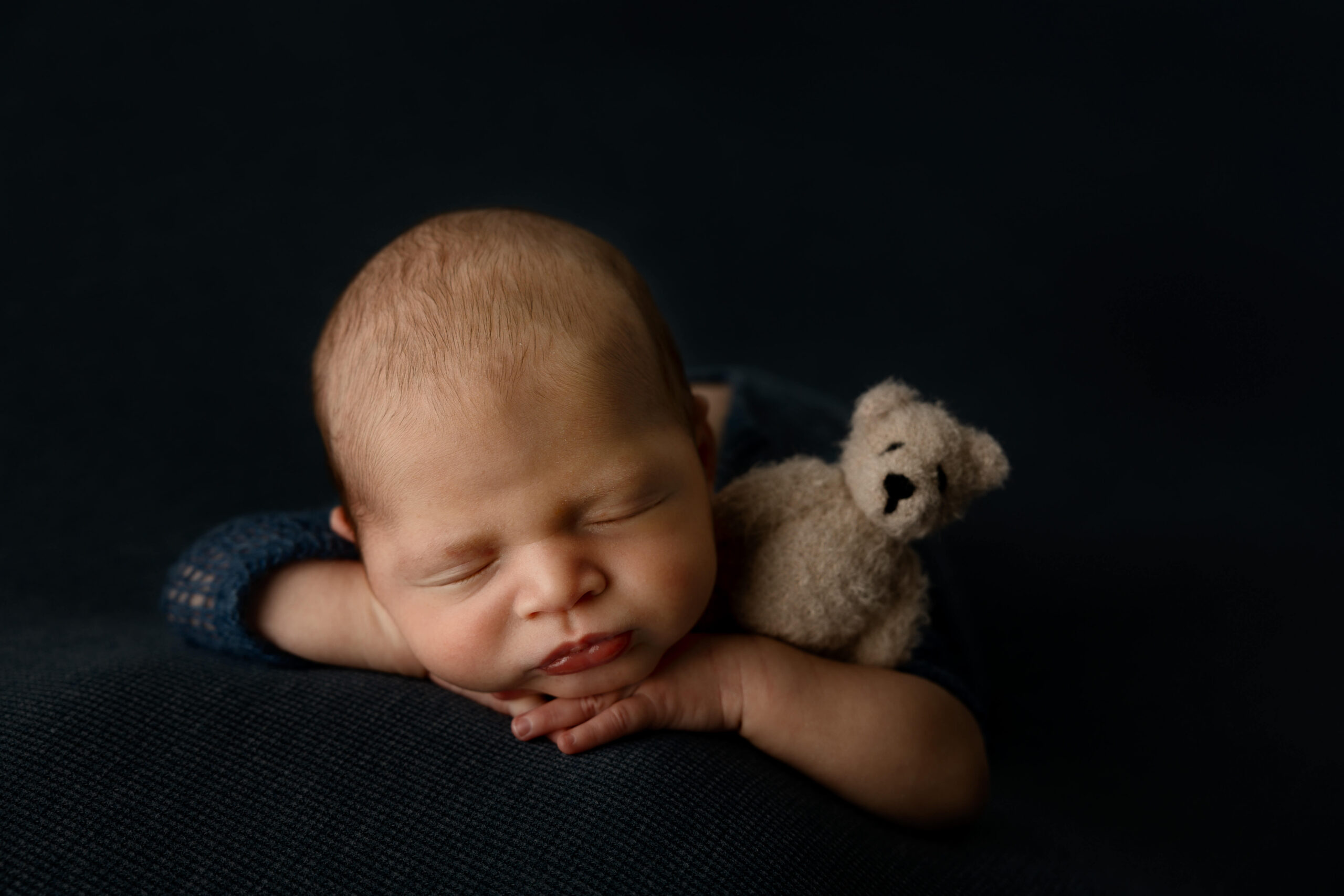 A closeup of a sleeping newborn baby holding a felt bear