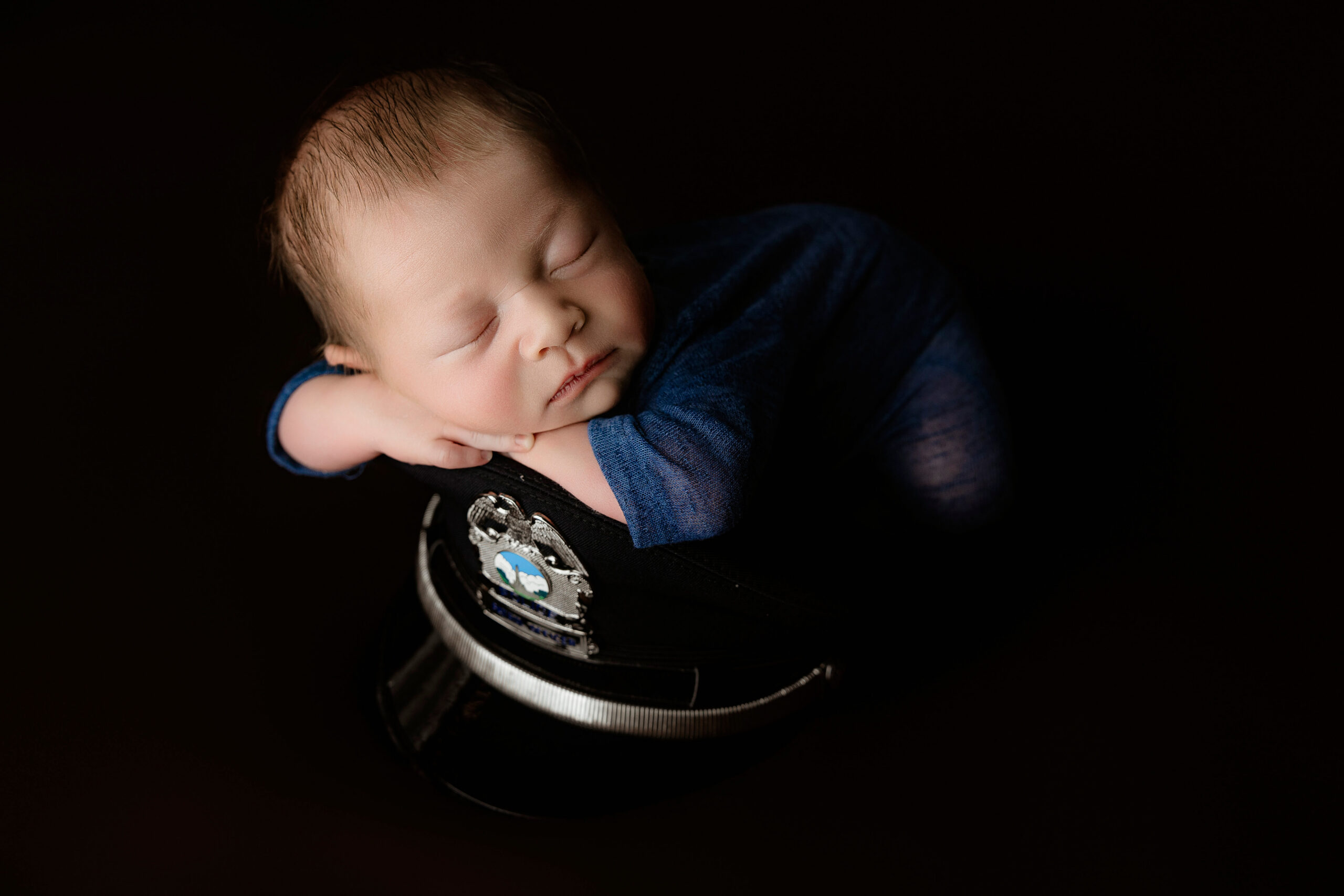 A newborn baby boy sleeps on a uniform cap in a blue onesie thanks to excellent birthing classes in peoria il
