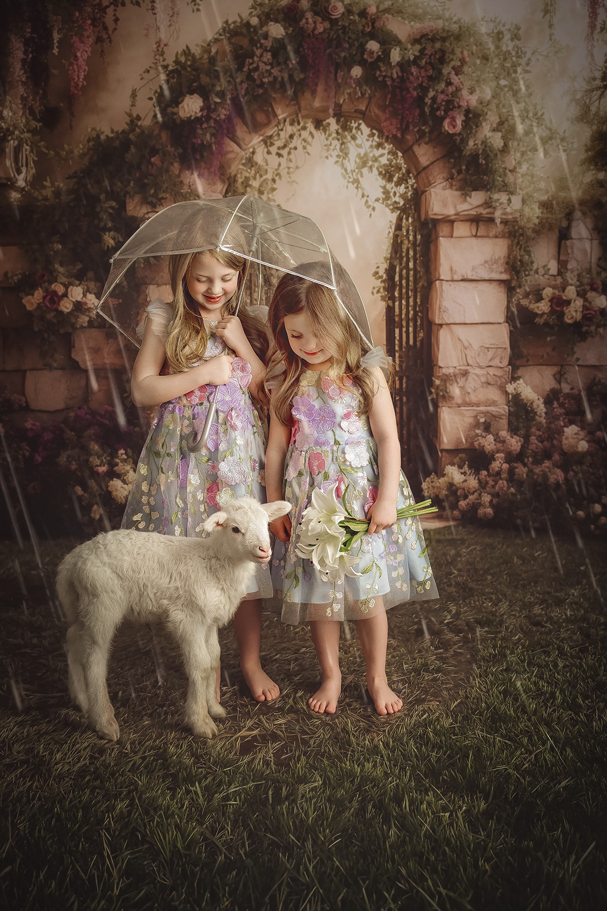 Toddler sisters in matching flower gown stand with a baby sheep in a studio holding flowers and clear umbrella after visiting pediatric chiropractors in peoria il