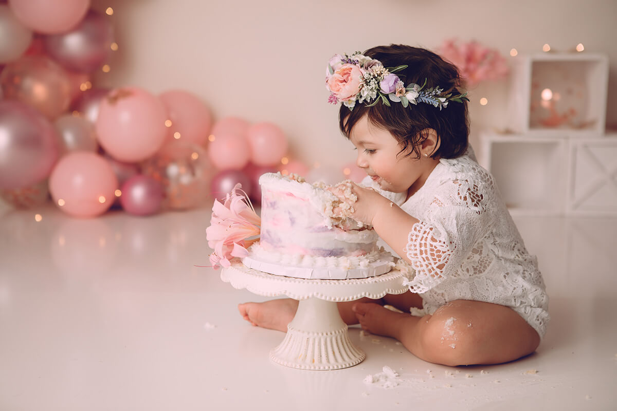 An excited baby girl in lace dives into a small cake for her birthday after some mommy and me classes in peoria, IL
