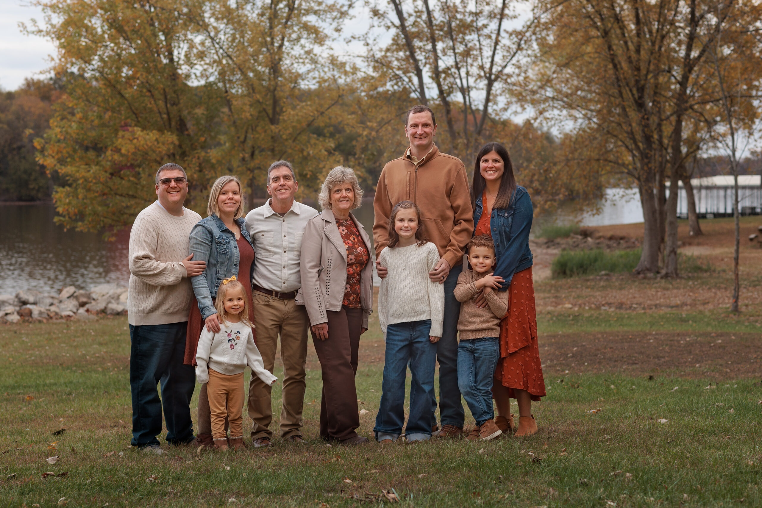 Smiling grandparents stand with their extended family by a pond in fall at sunset thanks to parenting classes in peoria, IL