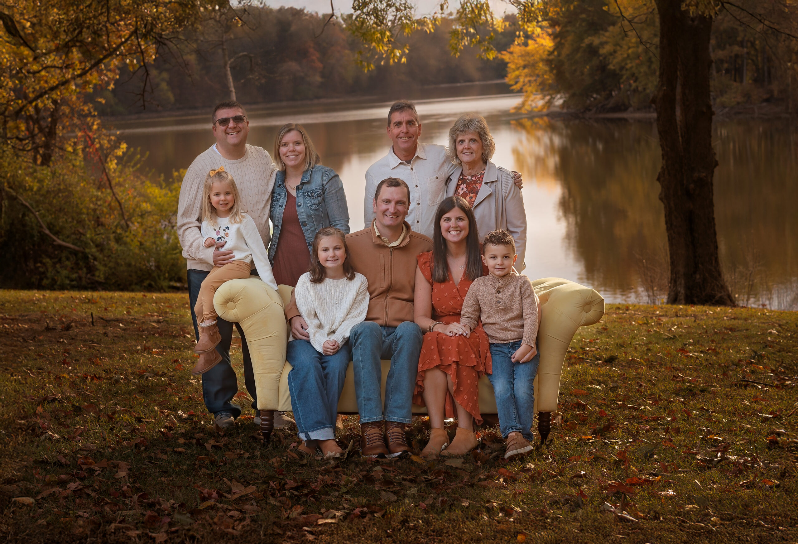 An extended family sits by the water on a couch at sunset with big smiles thanks to parenting classes in peoria, IL