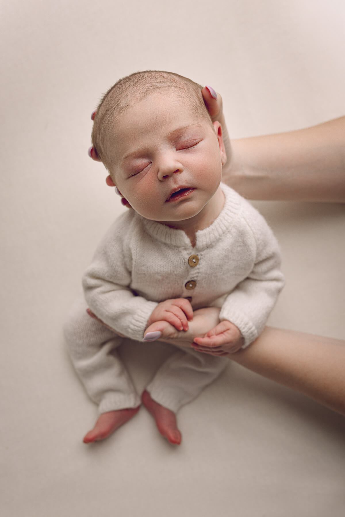 A mother holds the head of her sleeping newborn baby in a white onesie thanks to prenatal chiropractors in peoria il