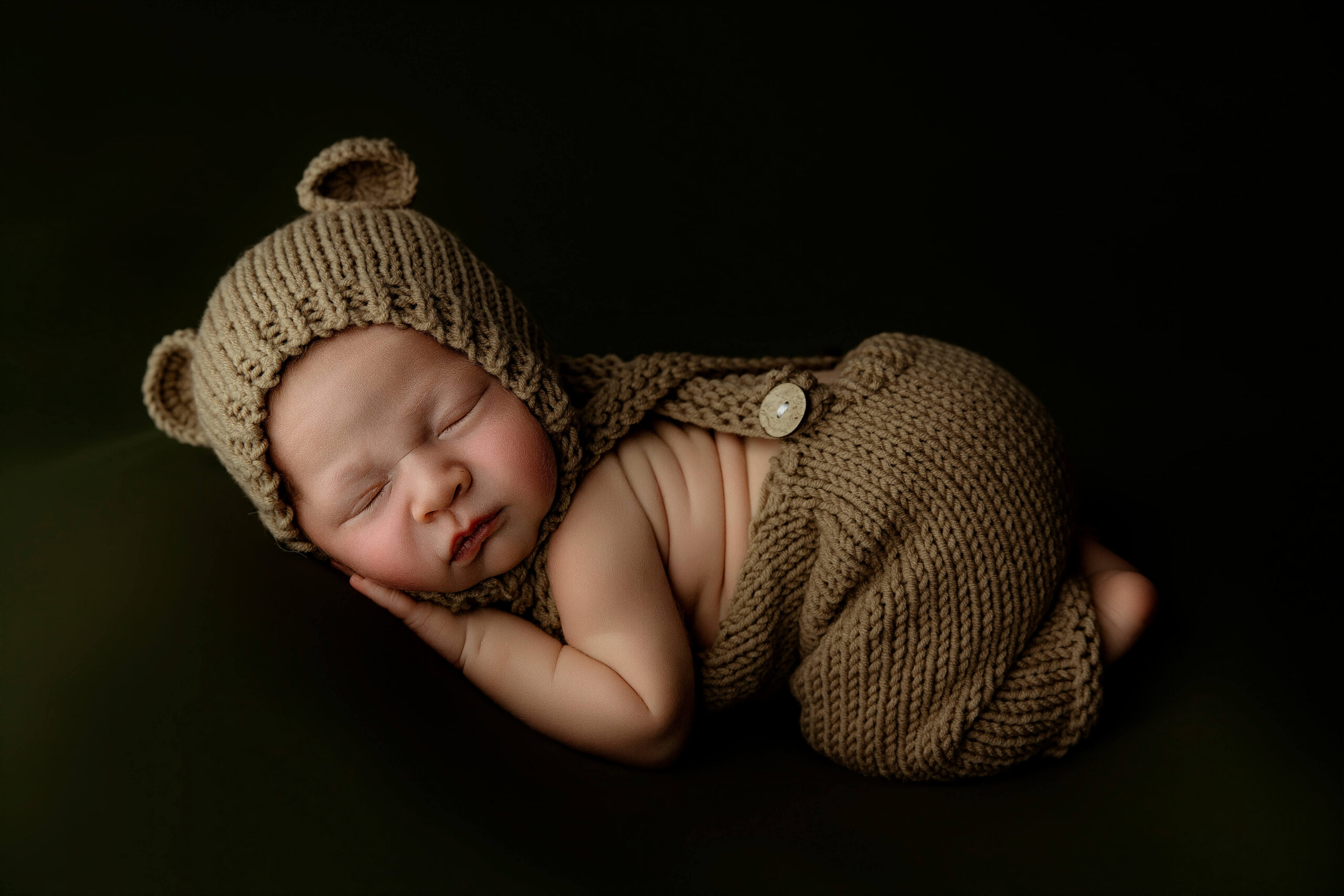 A newborn baby sleeps in brown knit overalls and matching teddy ears bonnet after mom enjoyed prenatal yoga in peoria il