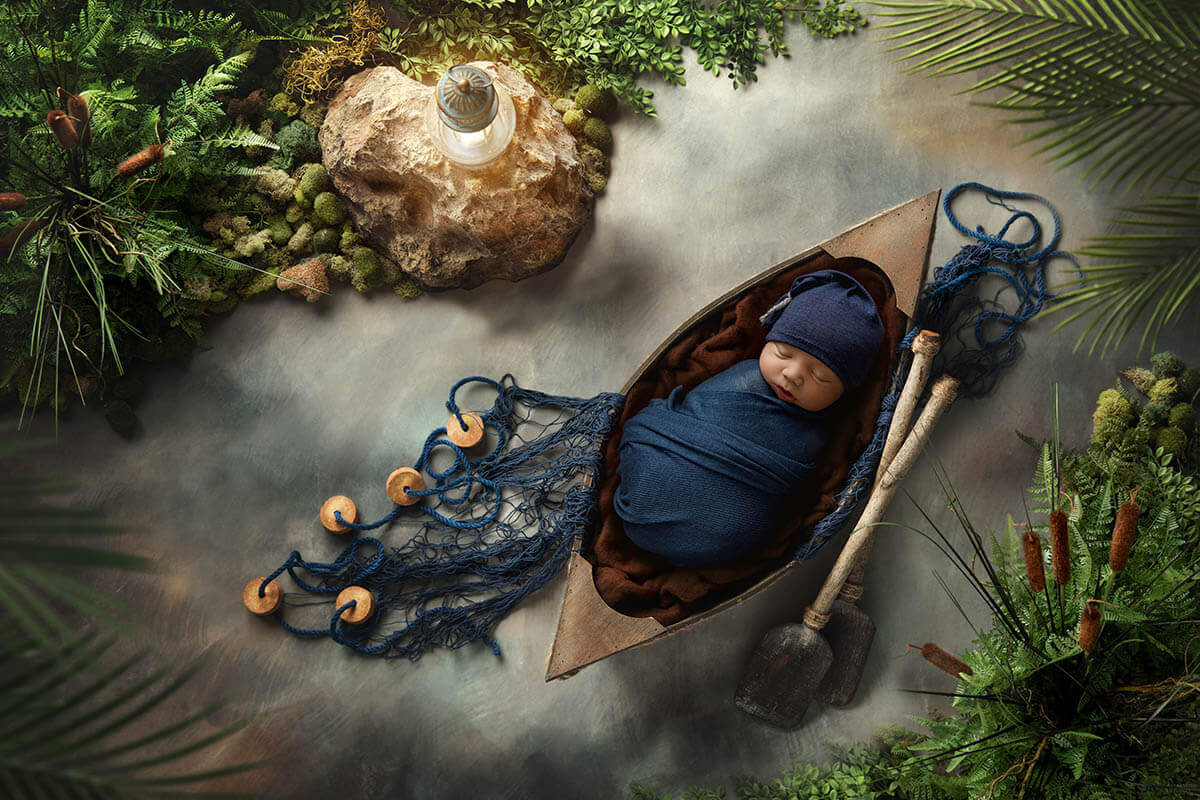 A newborn baby sleeps in a blue swaddle in a boat in a tropical river with net and paddles after mom enjoyed prenatal yoga in peoria il