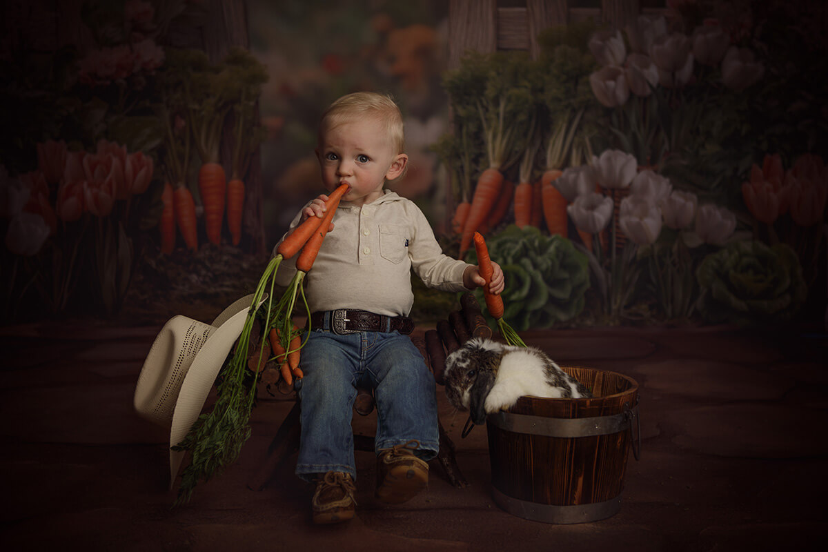A toddler boy bites into a carrot while sitting next to a bunny in a bucket in jeans after exploring preschools in Peoria, IL