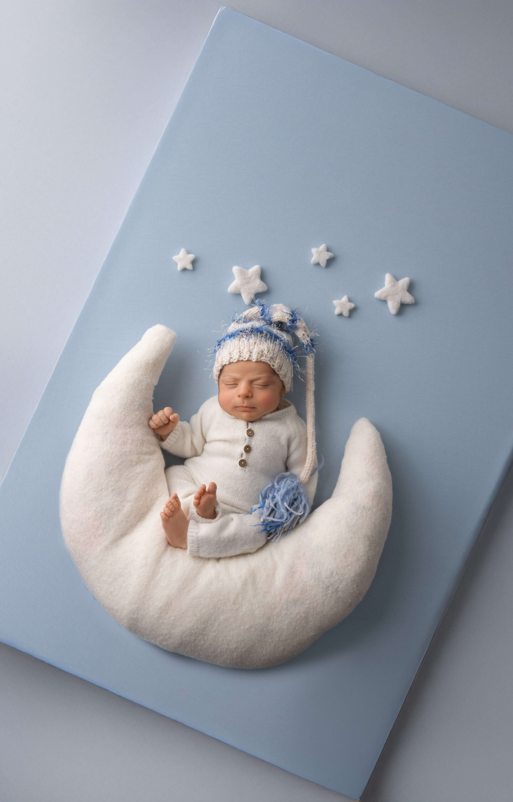 A baby sleeping in a white onesie and blue knit sleep cap on a felt stuffed moon after exploring daycares in champaign il
